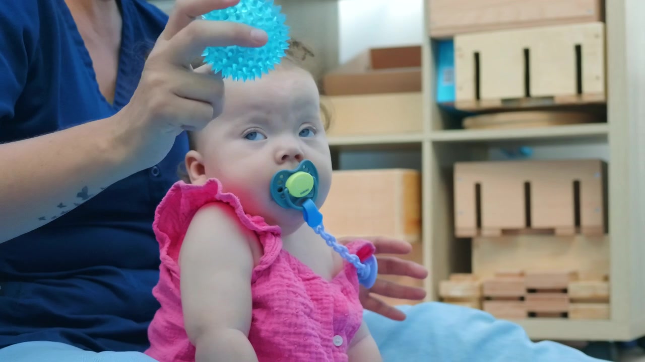 An adult holds a spiky sensory ball near a baby girl's face