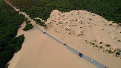 High-up-aerial-view-of-cars-slowly-commuting-on-a-very-sandy-road-off-the-coast-of-Spain