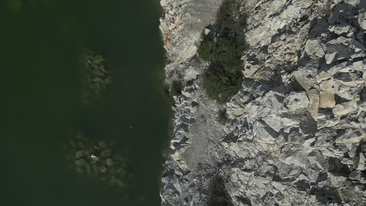 Aerial perspective revealing verdant quarry water intersecting rugged rocky terrain, showcasing dramatic natural color and textural contrasts of geological landscape