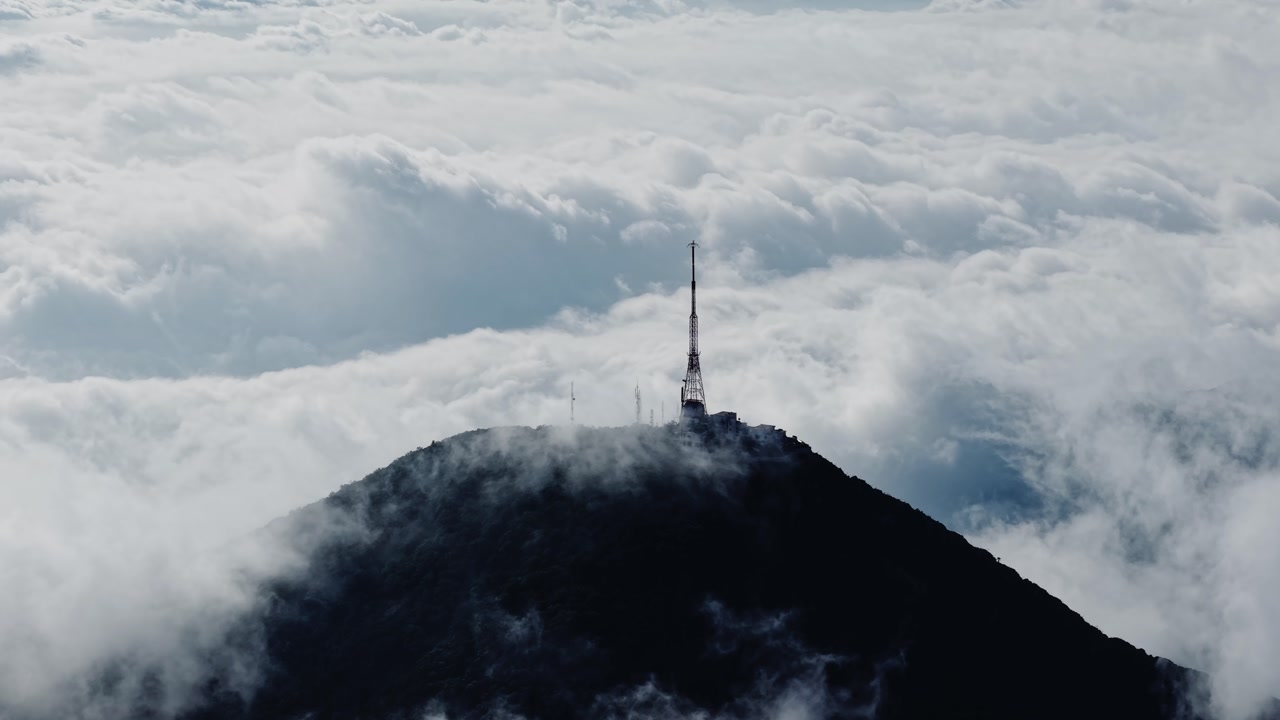 Aerial drone shot of communication tower on mountain peak surrounded by dense clouds showing elevation atmosphere and dramatic landscape