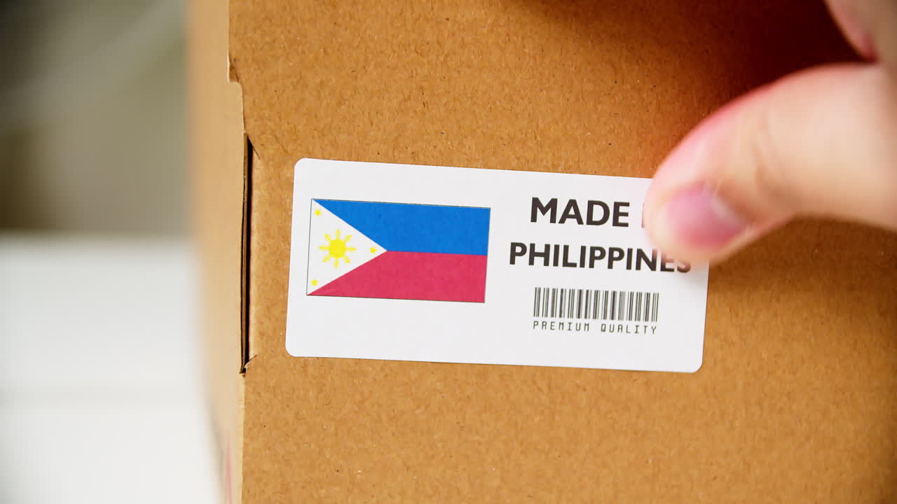 Hands applying MADE IN PHILIPPINES flag label on a shipping cardboard box with products. Close up shot with premium quality barcode