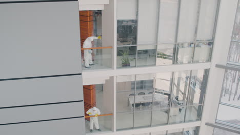 Distant-View-Of-Two-Cleaning-Men-Wearing-Personal-Protective-Equipment-Cleaning-Stair-Railings-Inside-An-Office-Building