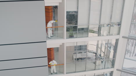 vista lejana de dos hombres de limpieza que usan equipo de protección personal limpiando barandillas de escaleras dentro de un edificio de oficinas