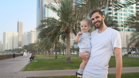 Padre-Jugando-Con-Sus-Hijos-En-El-Verano-En-Una-Ciudad-Moderna-Abrazándolo-Y-Abrazándolo-Con-Una-Camiseta-Blanca-Y-Pantalones-Cortos