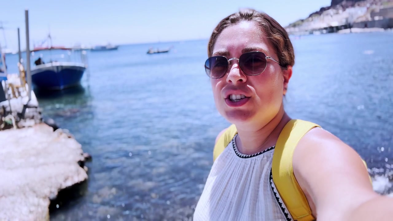 Giovane vlogger donna in streaming dalla spiaggia rossa di Santorini.