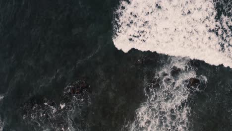 breathtaking top aerial view of dark blue ocean and giant waves crashing at rocky cliff with splashing and white foam