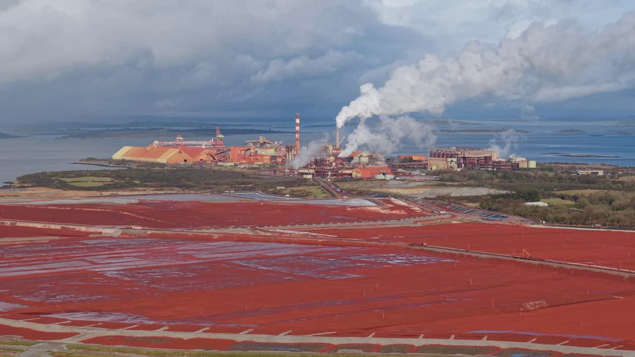 Russian-owned Aughinish Alumina refinery with red sludge waste, smoke, and factory view