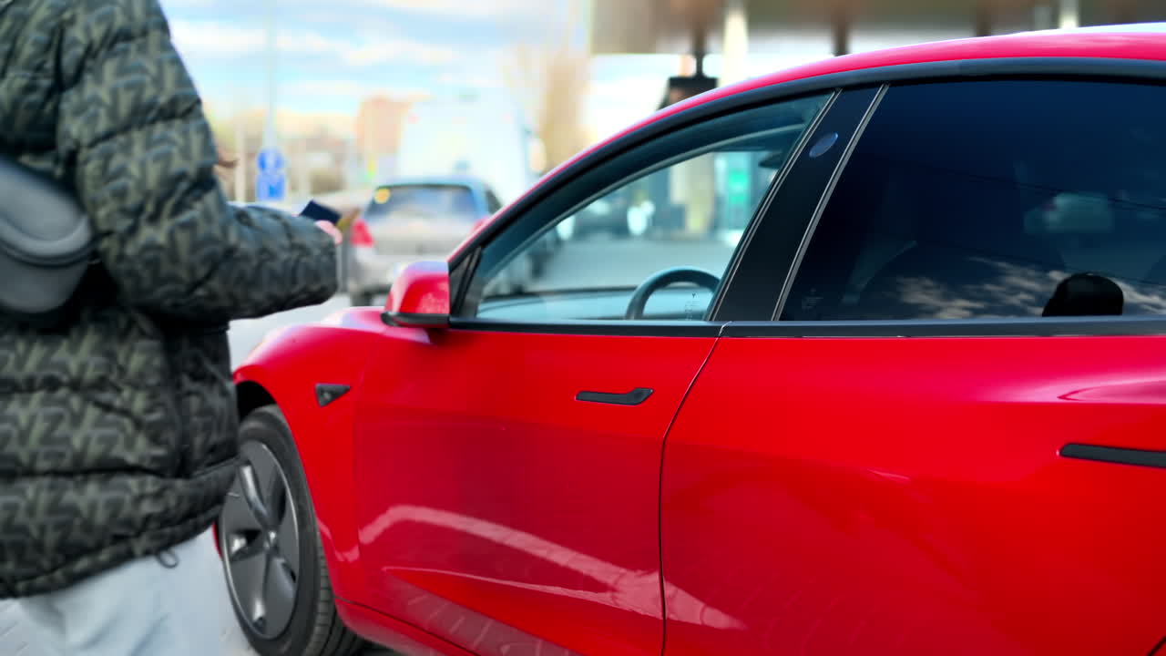 Primo piano di una donna che apre la sua auto elettrica rossa con una tessera e sale a bordo