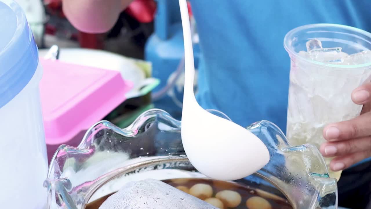 En gadesælger skovler søde longanfrugter og sirup i en plastik kop med is