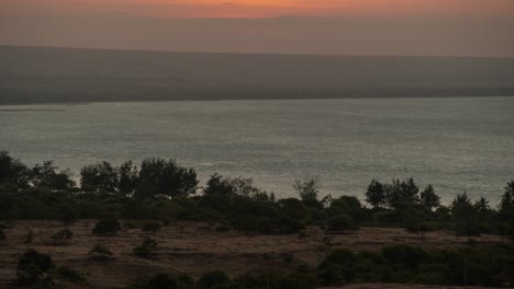 sunset over a tranquil bay with a distant horizon and silhouetted trees