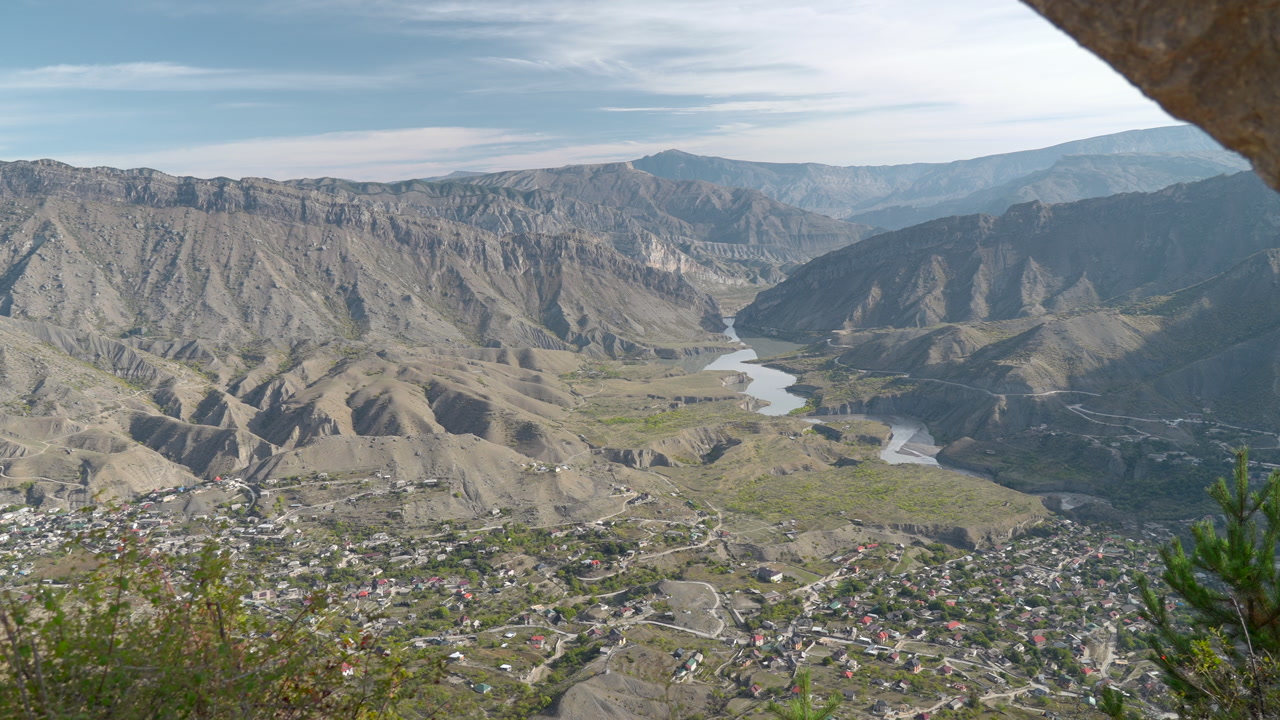 River Meander Cutting Through Steep Canyon From Rocky Overhang, Panoramic Town In Valley Below And Winding