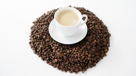 cup of coffee surrounded with roasted beans