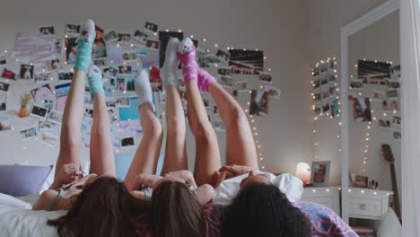 happy teen girls lying on bed at home with legs up having fun wiggling feet hanging out wearing pajamas enjoying relaxing morning on weekend