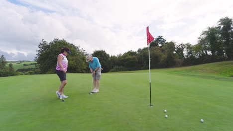 Male and female golf players playing golf and knocking golf ball into cup on golf course