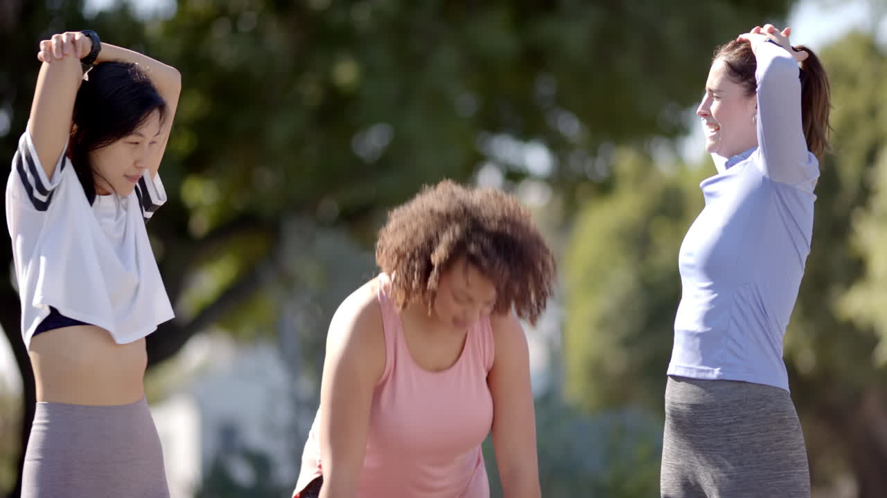 Stretching outdoors, three women friends in athletic wear preparing for workout