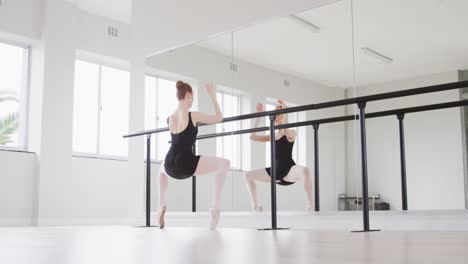 caucasian female ballet dancer stretching up by the mirror in a bright studio