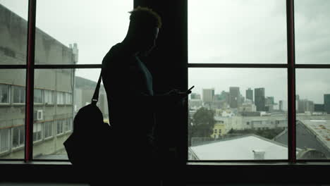 silhouette of a man using a mobile phone in front of a window with a cityscape