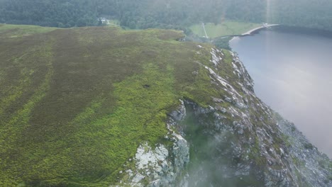 Nubes-Atrapadas-En-El-Acantilado-Rocoso-En-Las-Montañas-De-Wicklow-Con-El-Pintoresco-Lough-Tay,-Lago-Guinness-En-El-Condado-De-Wicklow,-Irlanda