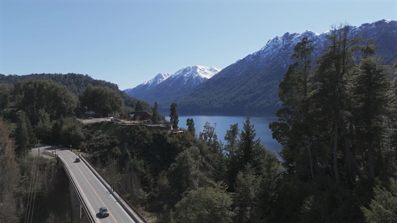 Ascesa aerea lenta sopra il Ponte sul fiume Correntoso, Lago Nahuel Huapi, con il Cerro Belvedere e il Cerro Inacayal innevati.