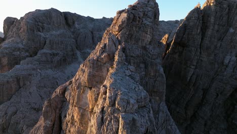 dynamic aerial tracking shot over the dolomites' rock formations, capturing the moment when the first sun rays touch the mountain summits