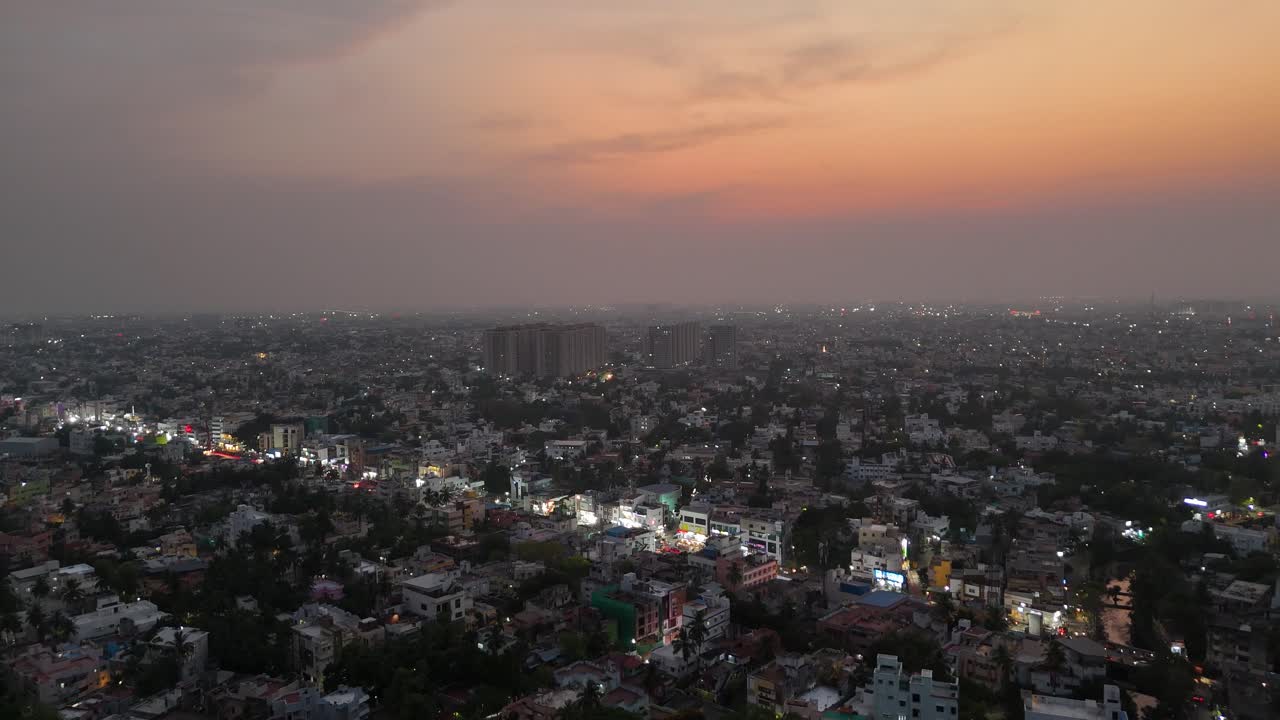 Aerial footage of Chennai at dusk. The city lights begin to shine against a beautiful orange and pink sky. Ideal for showcasing city life and urban transition