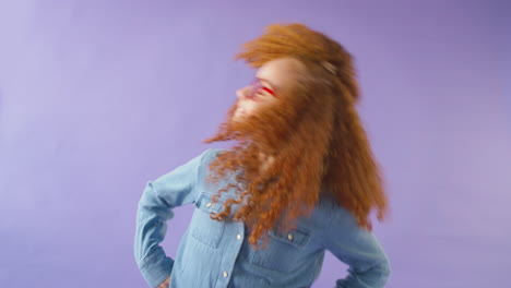 studio shot of young girl with red hair and glasses shaking hair against purple background