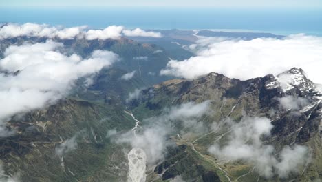 cámara lenta: toma aérea desde un vuelo panorámico sobre el glaciar fox de la costa oeste, el monte aoraki cook, el parque nacional con nubes, las montañas rocosas nevadas y el océano en el fondo