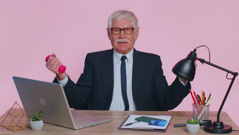 hombre de negocios senior haciendo ejercicio, bombeando los músculos de los brazos levantando pesas rosas, relajándose después del trabajo