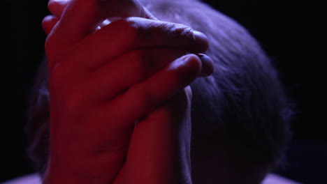 anxious individual joins hands together in prayer to god, lit by red top light