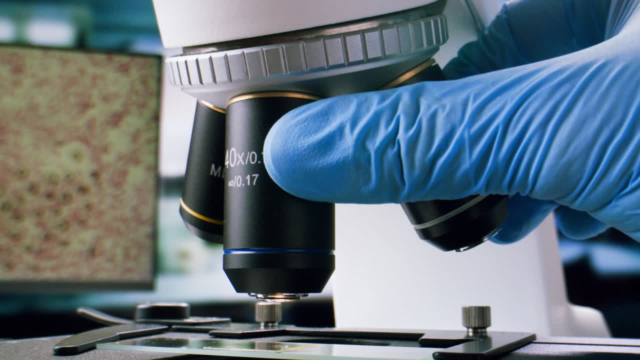 Gloved Hand Adjusting Microscope Objective Lens in Laboratory