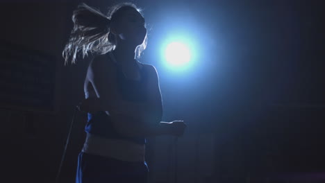 entrenando a una chica luchadora saltando la cuerda en una habitación oscura a la luz de una linterna