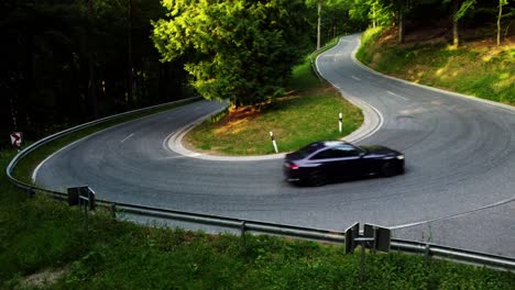 drone shot of a car driving dynamically through a sharp turn in a green forest in summer