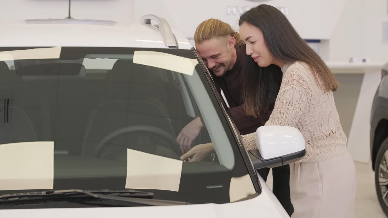 아름다운 젊은 부부는 자동차 전시장에서 새로운 자동차를 선택하고 있습니다.