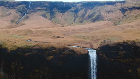 Vista-Aérea-Hacia-Atrás-De-Una-Montaña-Escarpada-Con-Una-Cascada