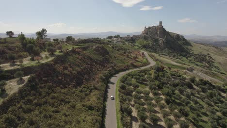 drone siguiendo un coche que conduce hacia las antiguas ruinas de craco en una colina en el sur de italia en 4k