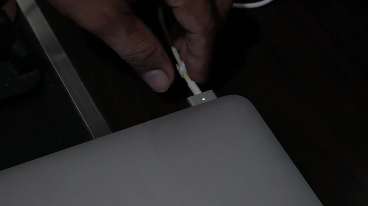 Close-Up of Hand Unplugging Power Charger Cable from Laptop