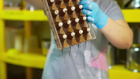 chocolatier turned over the molds filled with chocolate. confectioner getting rid of extra chocolate with spatula. the trickles of black liquid chocolate fall downwards.