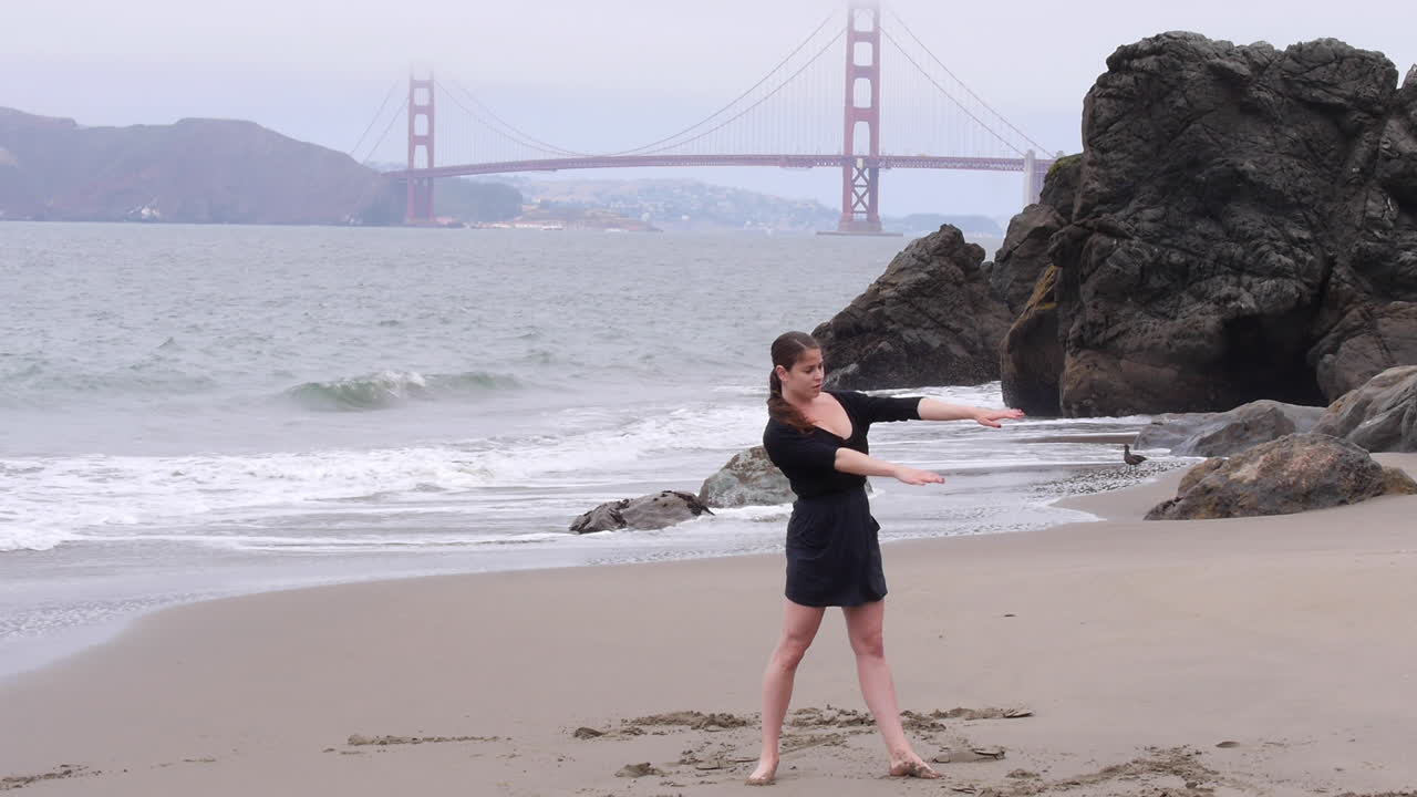 와이드 샷, 여성은 극적인 표현, 안개 낀 해변의 날을 사용하여 해석적으로 춤을 춥니다.