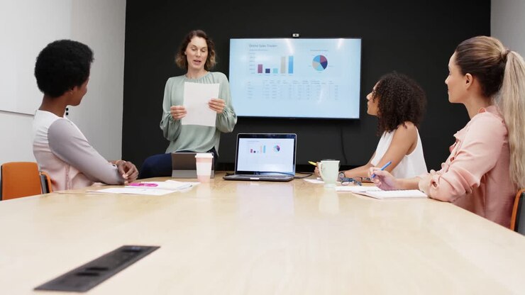 Empresarias diversas haciendo una presentación en una reunión de oficina, usando una laptop y una tableta, en cámara lenta.