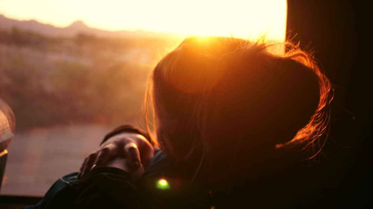 female traveler looks out a window into sunrise and puts her head to rest on bnackpoack