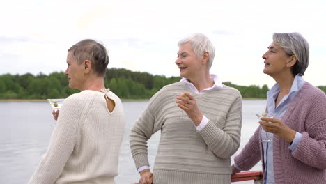 three senior women having a drink close to a lake