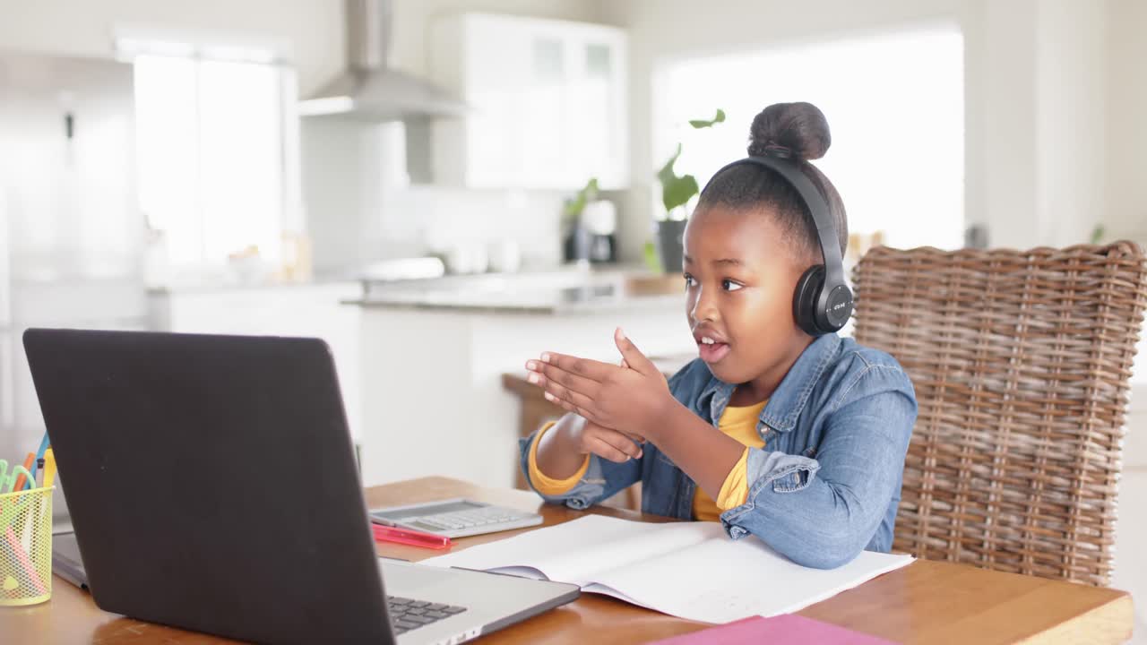 Happy unaltered african american girl using laptop and headphones for online lesson, in slow motion