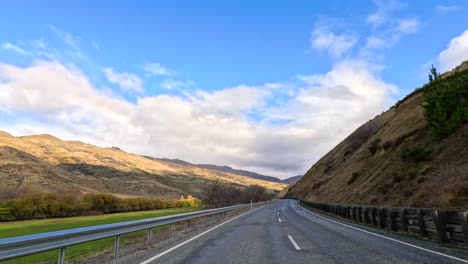 a serene drive through wanaka's winding roads, showcasing stunning mountain views under a bright blue sky