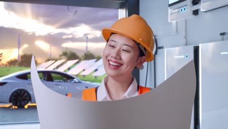 close up of asian female engineer with safety helmet looking at blueprint in her hands with home energy storage system in a modern garage
