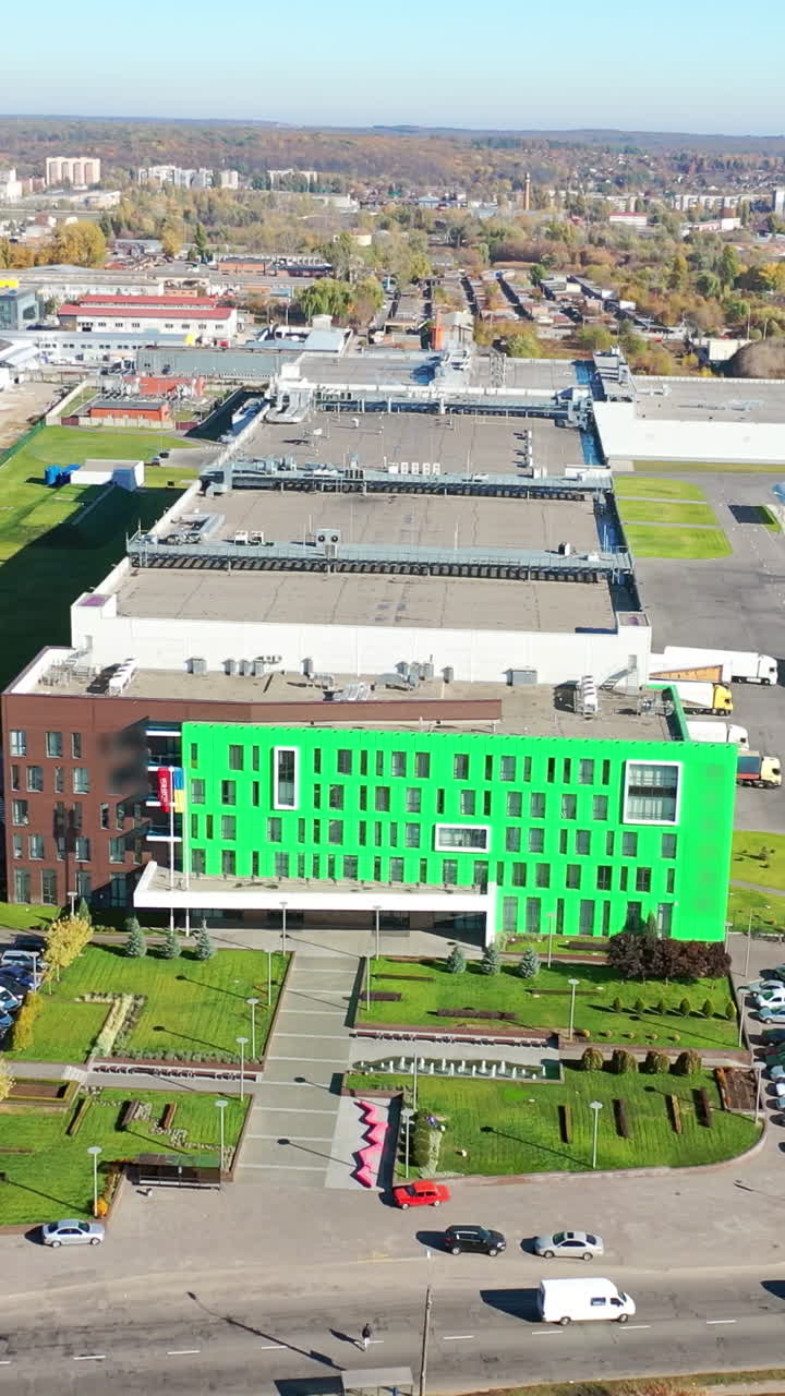 Big factory from bird's eye view. Exterior of a modern plant with many parking places. Contemporary complex on the city background. Aerial view. Vertical video