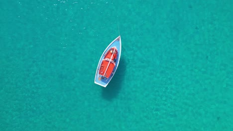 Slow-aerial-descend-above-colorful-sailboat-anchored-in-crystal-clear-water,-top-down