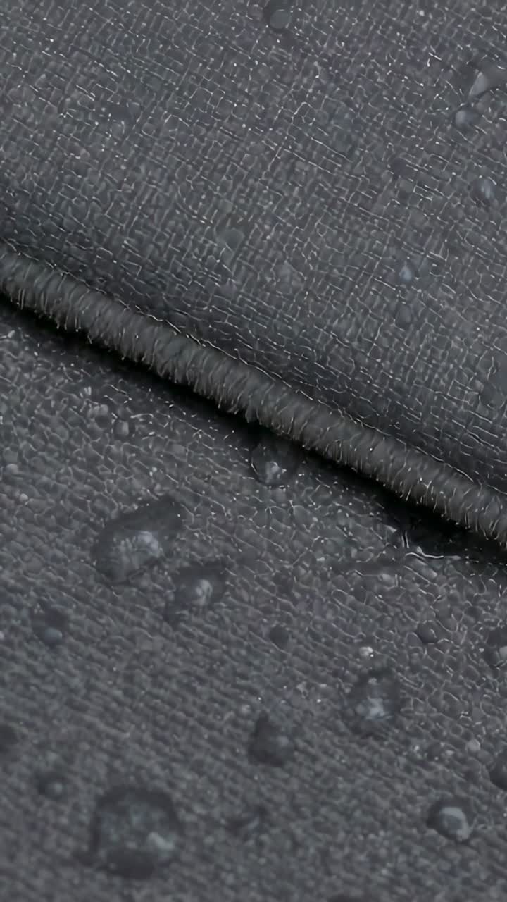 Vertical video: Panning macro camera revealing folded seam fabric in studio, showing water beading