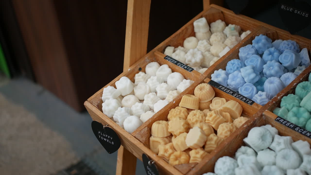 Wooden display showcases pastel-colored wax melts in various shapes, organized by scent