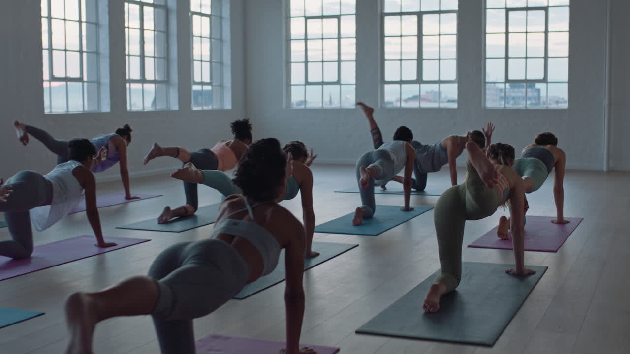 yoga class of healthy women practicing one-legged downward facing dog pose enjoying exercising in fitness studio instructor leading group meditation teaching workout posture at sunrise