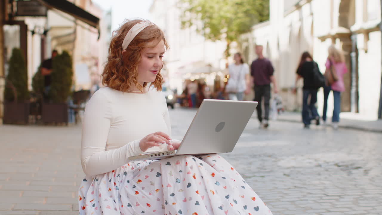 Woman freelancer working online distant job with laptop sitting in city street browsing website